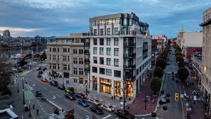 A modern building with multiple floors and large windows, situated in a busy urban area with a river and other buildings in the background. - Harbour Heaven (Victoria)