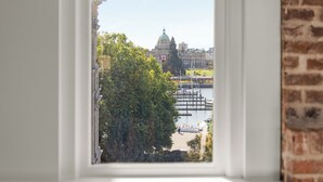 A view through a window of a building with a brick wall, a large tree, and a body of water with boats. - Harbour Heaven (Victoria)