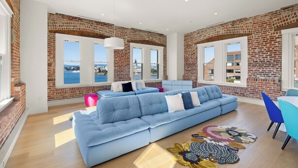 A spacious living room with a blue sofa, a coffee table, and a view of the sea through large windows. - Harbour Heaven (Victoria)