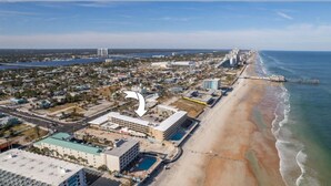 An aerial view of a coastal city with a beachfront hotel, a pier, and a mix of residential and commercial buildings. - Charming apartment in serene Daytona Beach with AC (Daytona Beach)