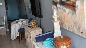 A room with a painting of boats on the wall, a small lighthouse model, a table with a chair, and a television mounted on the wall. - Charming apartment in serene Daytona Beach with AC (Daytona Beach)