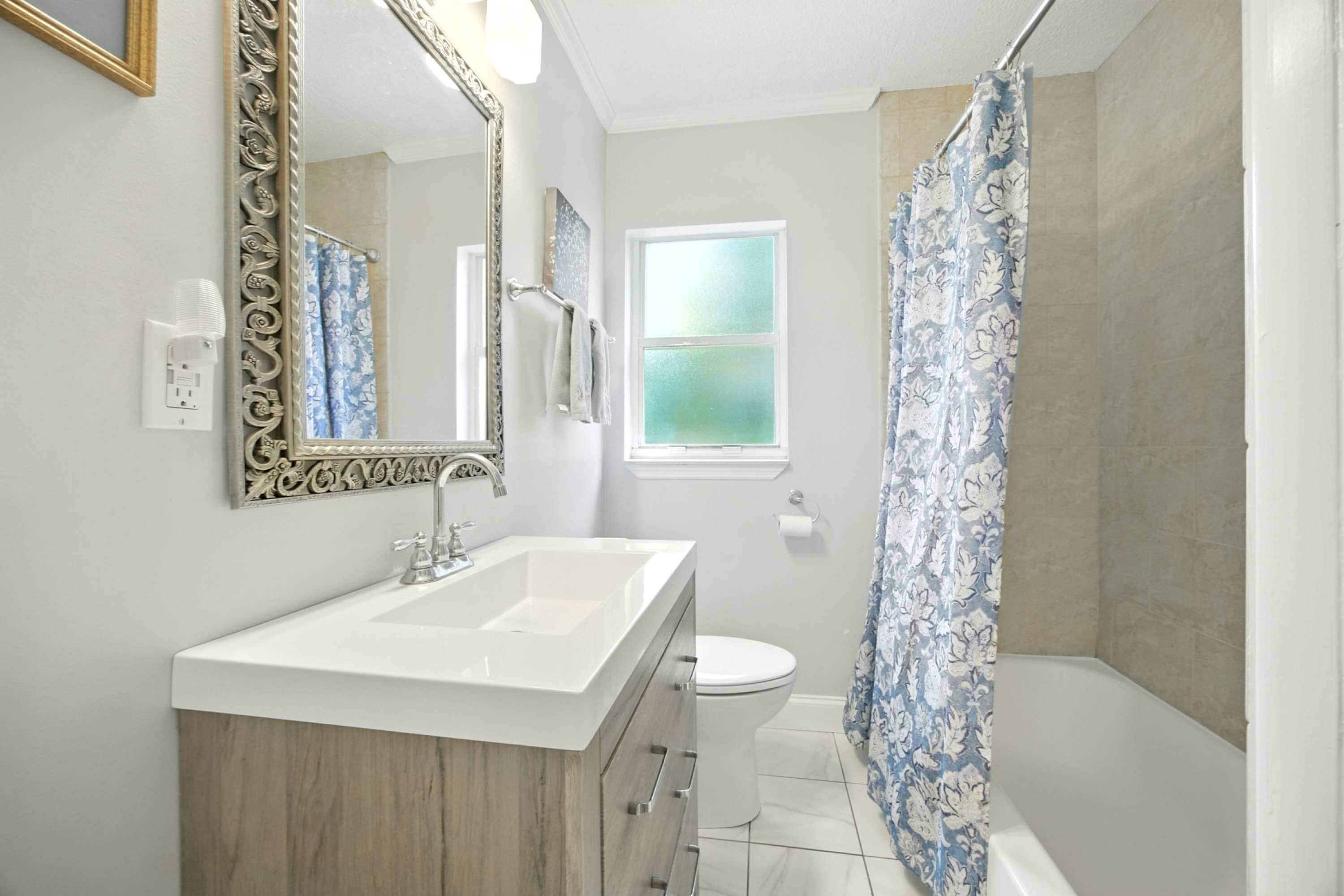 Un baño con lavamanos blanco, tocador de madera, inodoro y ducha con cortinas estampadas.
