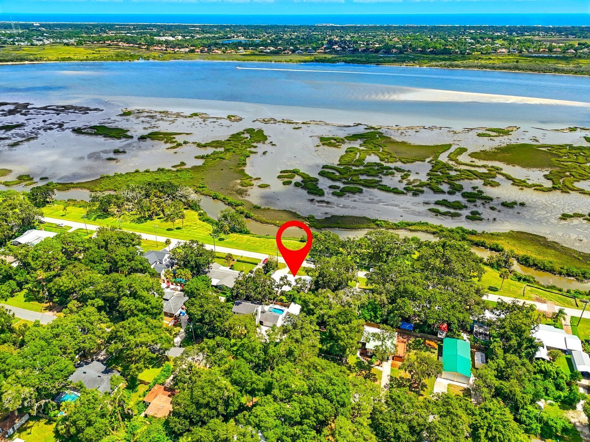 An aerial view of a coastal area with a marked location, surrounded by lush greenery and a large body of water.