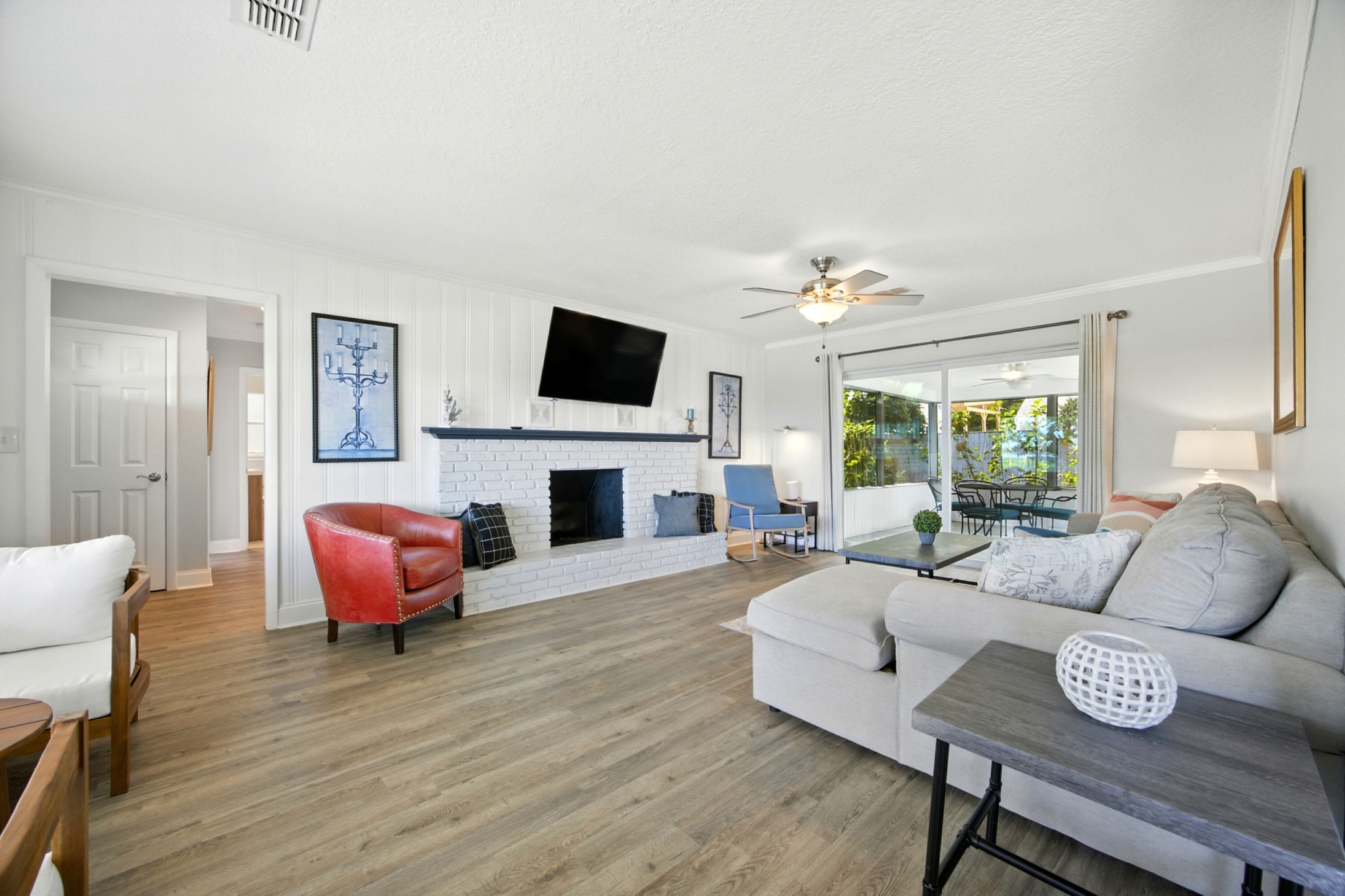 A living room with a fireplace, a sofa, a red chair, a TV mounted on the wall, and a ceiling fan.