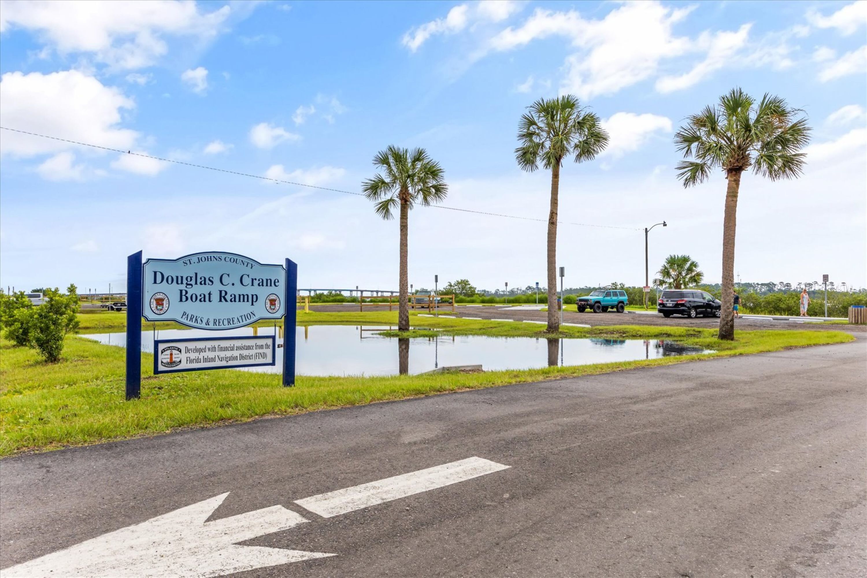 A sign for Douglas C. Crane Boat Ramp in St. Johns County, Florida, with a clear sky and palm trees in the background.