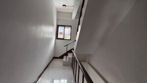 A narrow, white-walled stairwell with a handrail, leading to a landing with a window. - Asleep2 (Bangkok)
