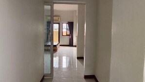 A hallway with a glass door leading to a room, a tiled floor, and a view of a balcony with a window and curtains. - Asleep2 (Bangkok)