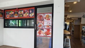A restaurant interior with a wooden floor, a glass door with menu posters, and a visible seating area with stools. - Asleep2 (Bangkok)