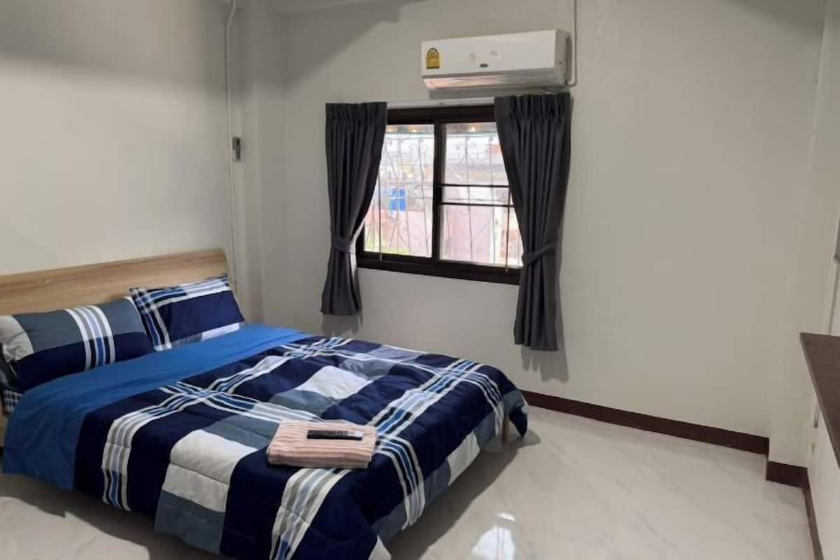 Un dormitorio con cama, ventana con cortinas, aire acondicionado y cabecero de madera.