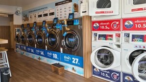 A laundromat with multiple washing machines and dryers, price signs, and a small stool. - Asleep2 (Bangkok)