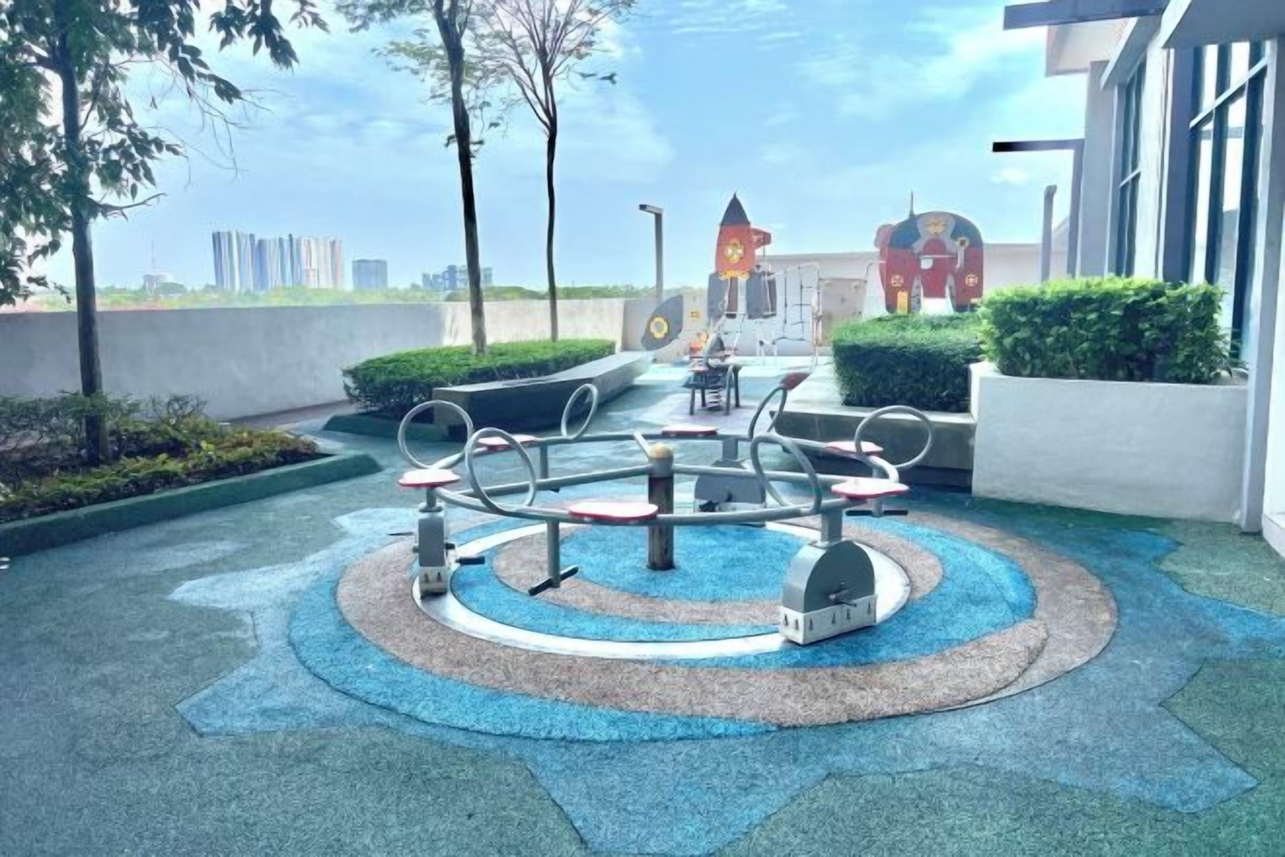 A playground with circular exercise equipment, surrounded by landscaped areas and a building in the background.