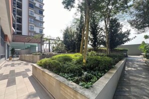 A courtyard with a checkered floor, a planter with greenery, and a tall building in the background.