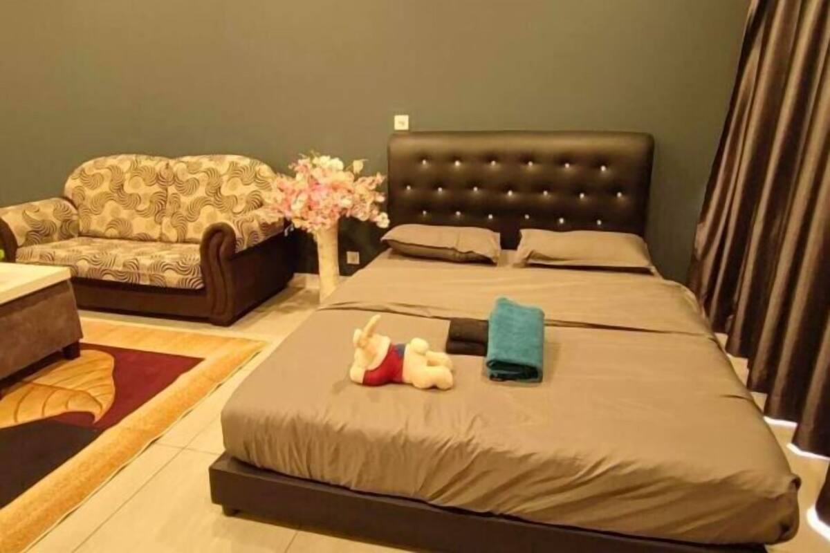 A hotel room with a bed, a sofa, a small table, and a decorative vase with flowers.