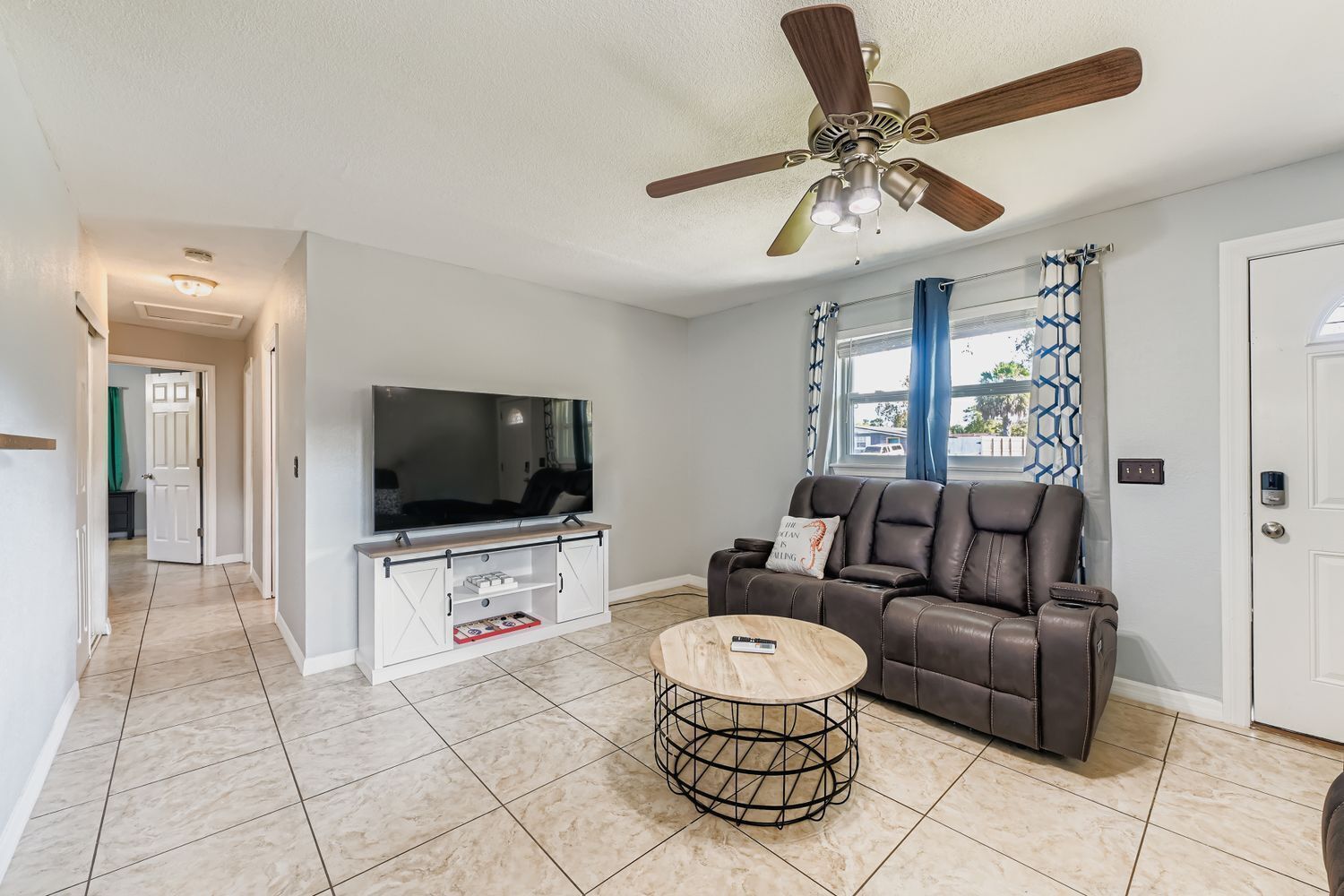 A living room with a TV, leather sofa, and a ceiling fan.