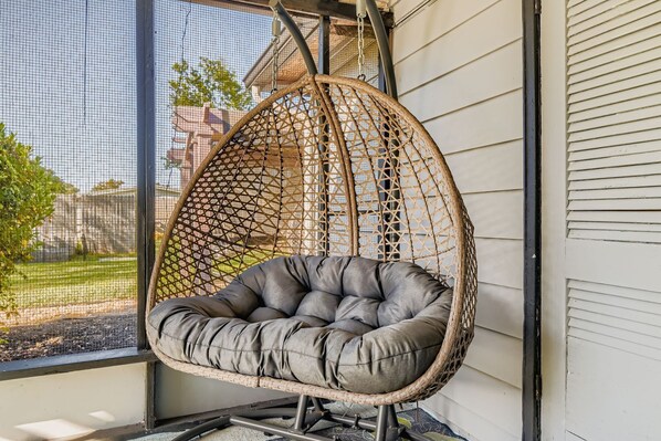 Une chaise suspendue dotée d’un siège et d’un dossier rembourrés, maintenue par une structure de cordes tressées, et placée contre la façade d’un bâtiment.