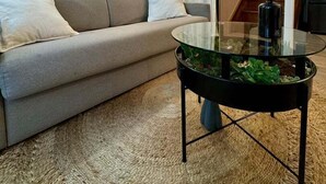 A modern living room with a grey sofa, a glass coffee table with plants, and a staircase in the background.