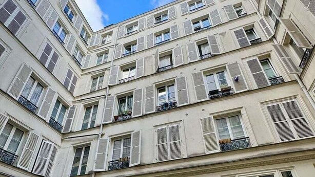 A multi-story building with balconies, a courtyard with potted plants, and a clear sky.