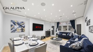 Una sala de estar moderna con comedor, un conjunto de sofás y un televisor de pantalla plana mostrando 'NETFLIX'.