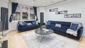 Una sala de estar moderna con dos sofás azules, una mesa de centro de vidrio y una alfombra gris.