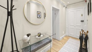 Un interior moderno con una mesa consola de vidrio, un espejo redondo y una puerta con perchero.