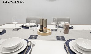 Mesa de comedor dispuesta con platos blancos, cubiertos y vasos, con un adorno central y un reloj de pared.
