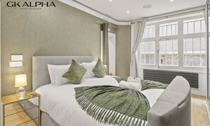 Una habitación de hotel moderna con una cama grande, una mesita de noche, una silla y un ventanal con cortinas.
