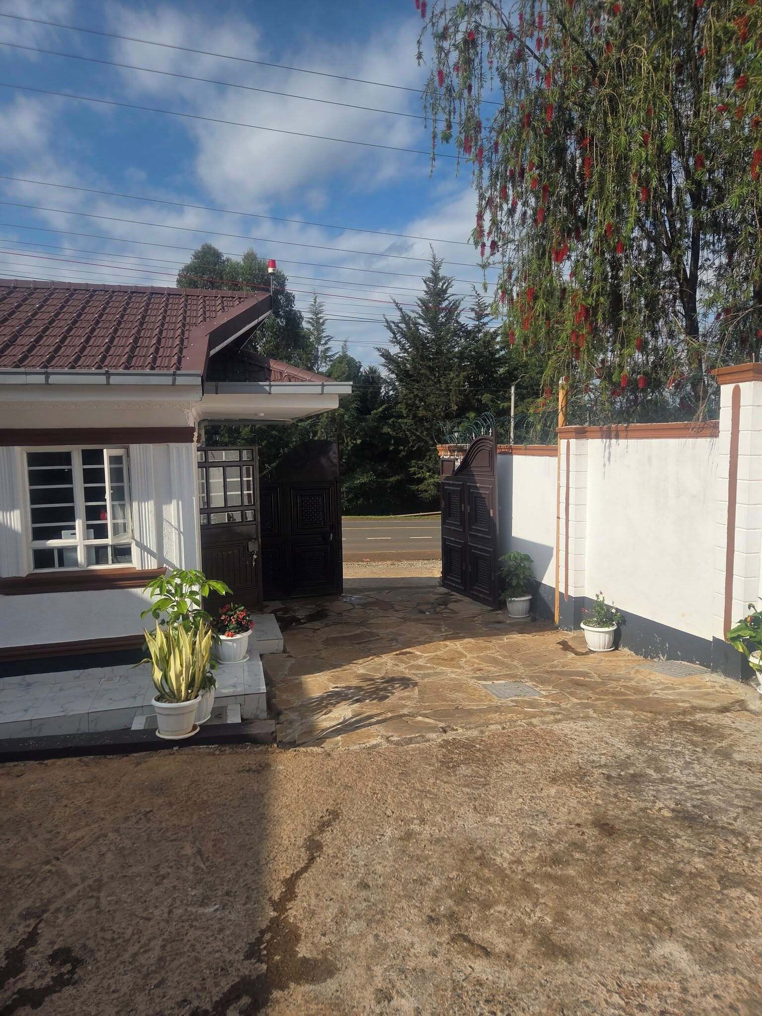 A house with a tiled roof, a gated entrance, and potted plants in the foreground.