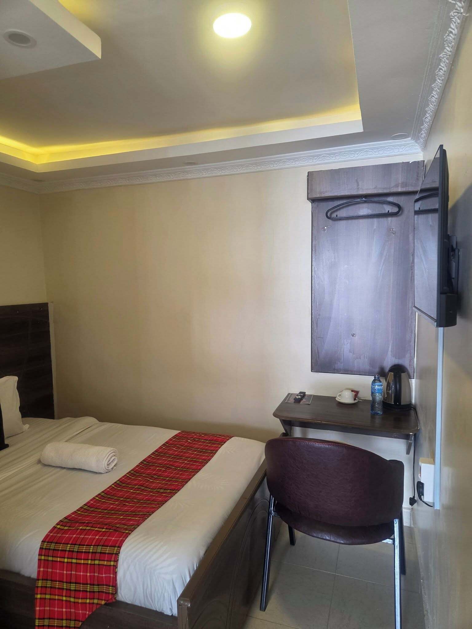 A hotel room with a bed, a desk, a chair, and a TV mounted on the wall.