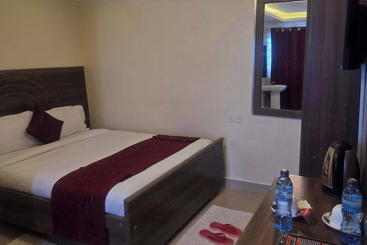 A hotel room with a bed, a small table with water bottles, a mirror, and a TV.