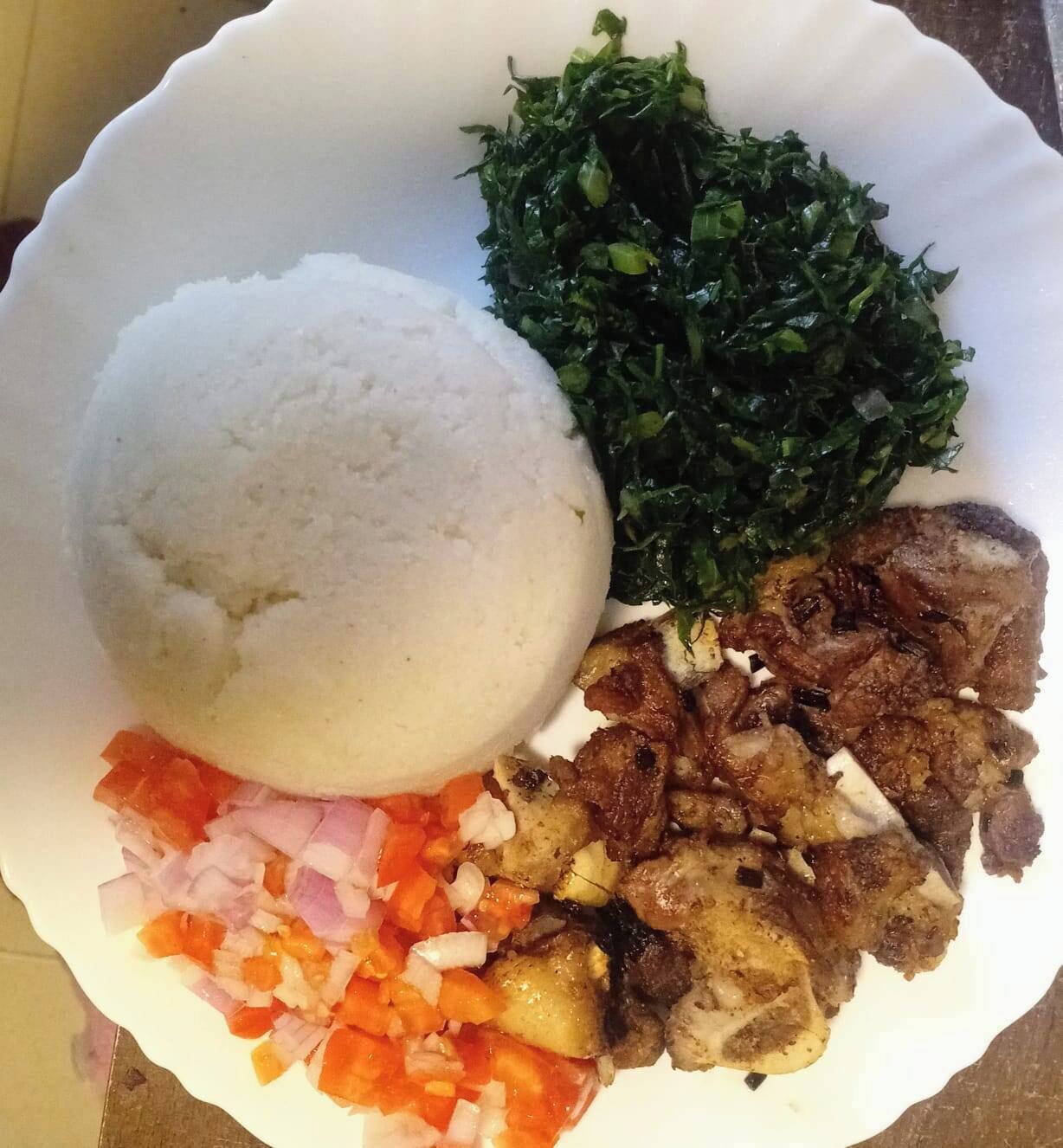 A plate with white rice, sautéed greens, diced carrots, and grilled meat.