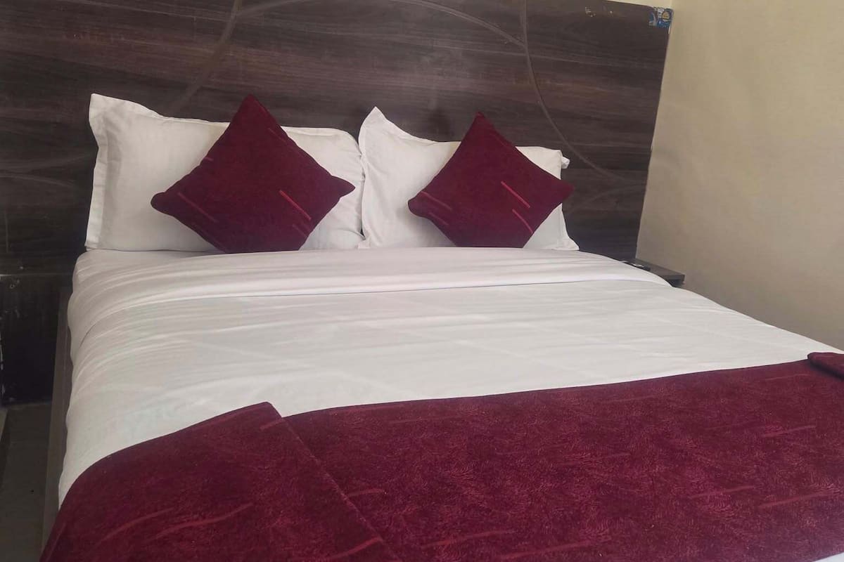 A neatly made bed with white linens and two dark red pillows, a dark wood headboard, and a red throw blanket.