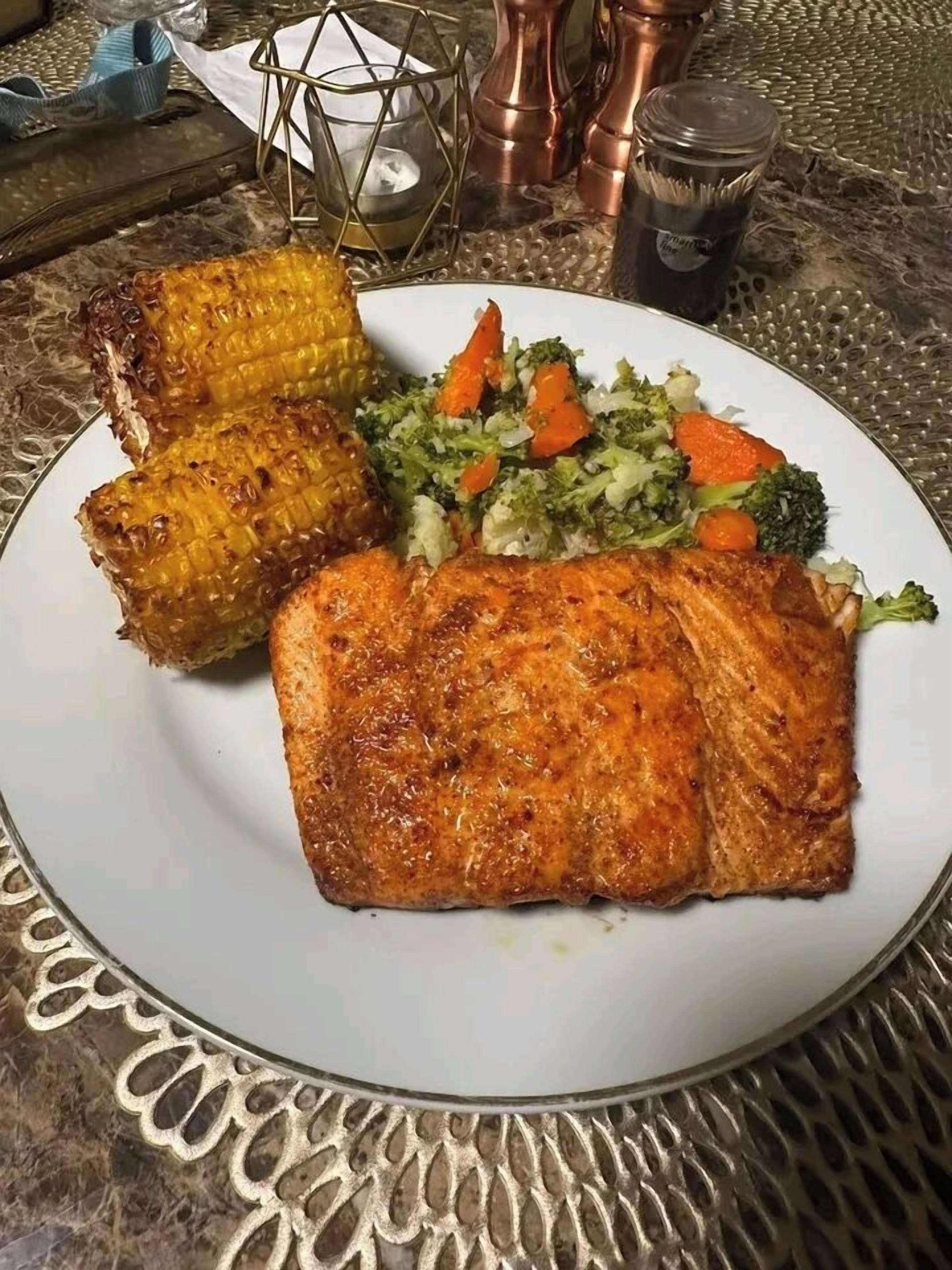 Une assiette comprenant du saumon grillé, des épis de maïs et un assortiment de légumes.