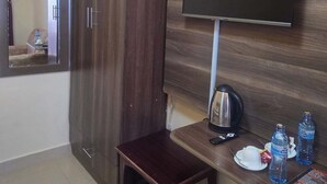A hotel room with a wooden wardrobe, a flat-screen TV mounted on the wall, a small wooden table with a kettle, and a mirror. - The Elegant Homes &Accommodation Kericho (Kericho)