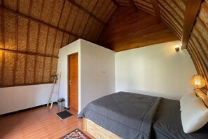 Een slaapkamer met een houten plafond, een bed met een grijze dekbedovertrek, een bedlampje en een klein vloerkleed.