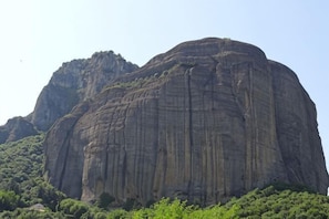 A large rock formation with a flat top and steep sides, surrounded by greenery.