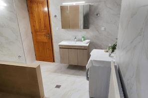 Un baño con puerta de madera, un lavamanos con espejo y una zona de ducha.