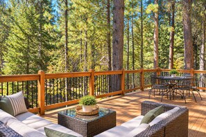 A deck with wicker furniture, a table, and a railing. - Black Butte Ranch House 007 (Sisters)