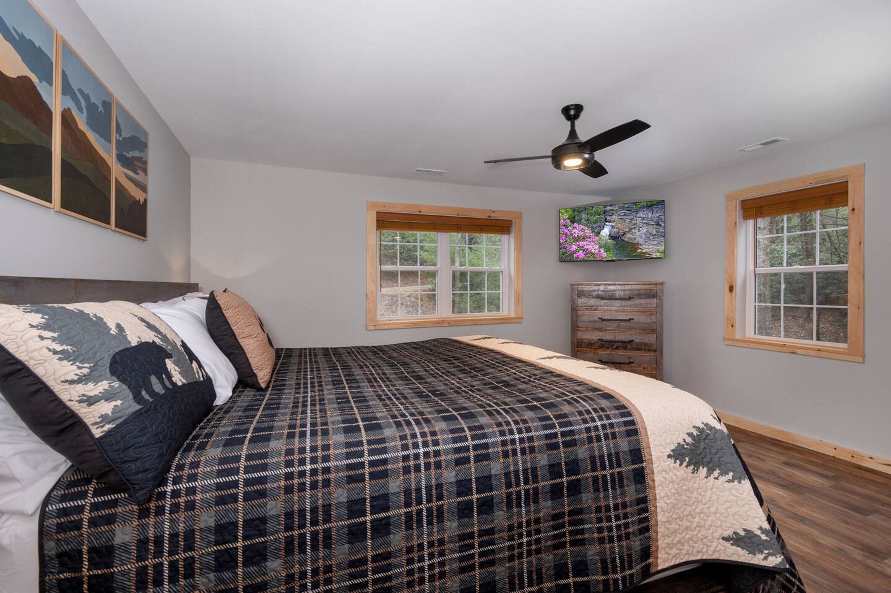 A bedroom with a bed, a ceiling fan, two windows, and a wooden dresser.