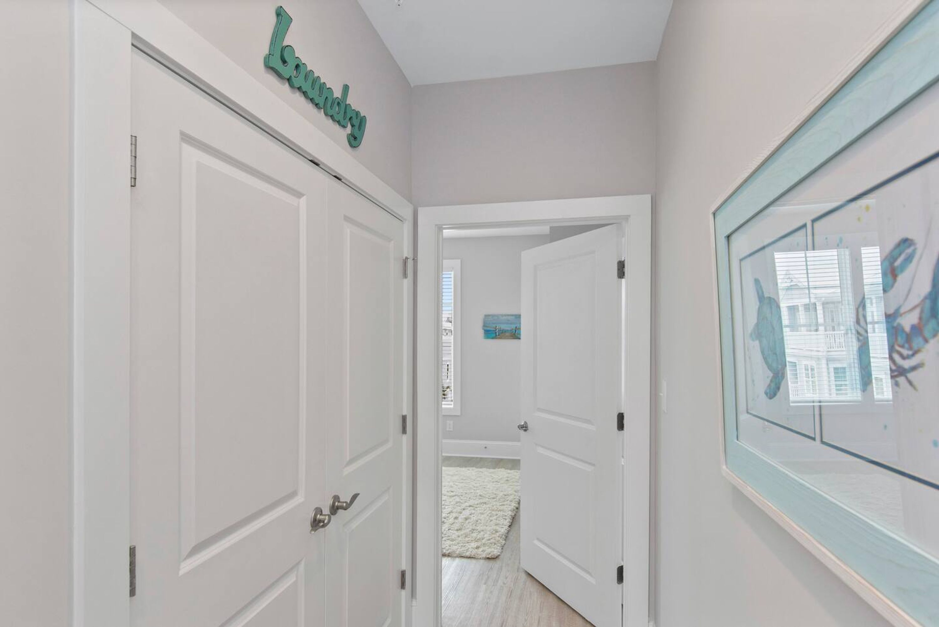 A hallway with white doors, a 'Laundry' sign above one door, and a framed picture on the wall.