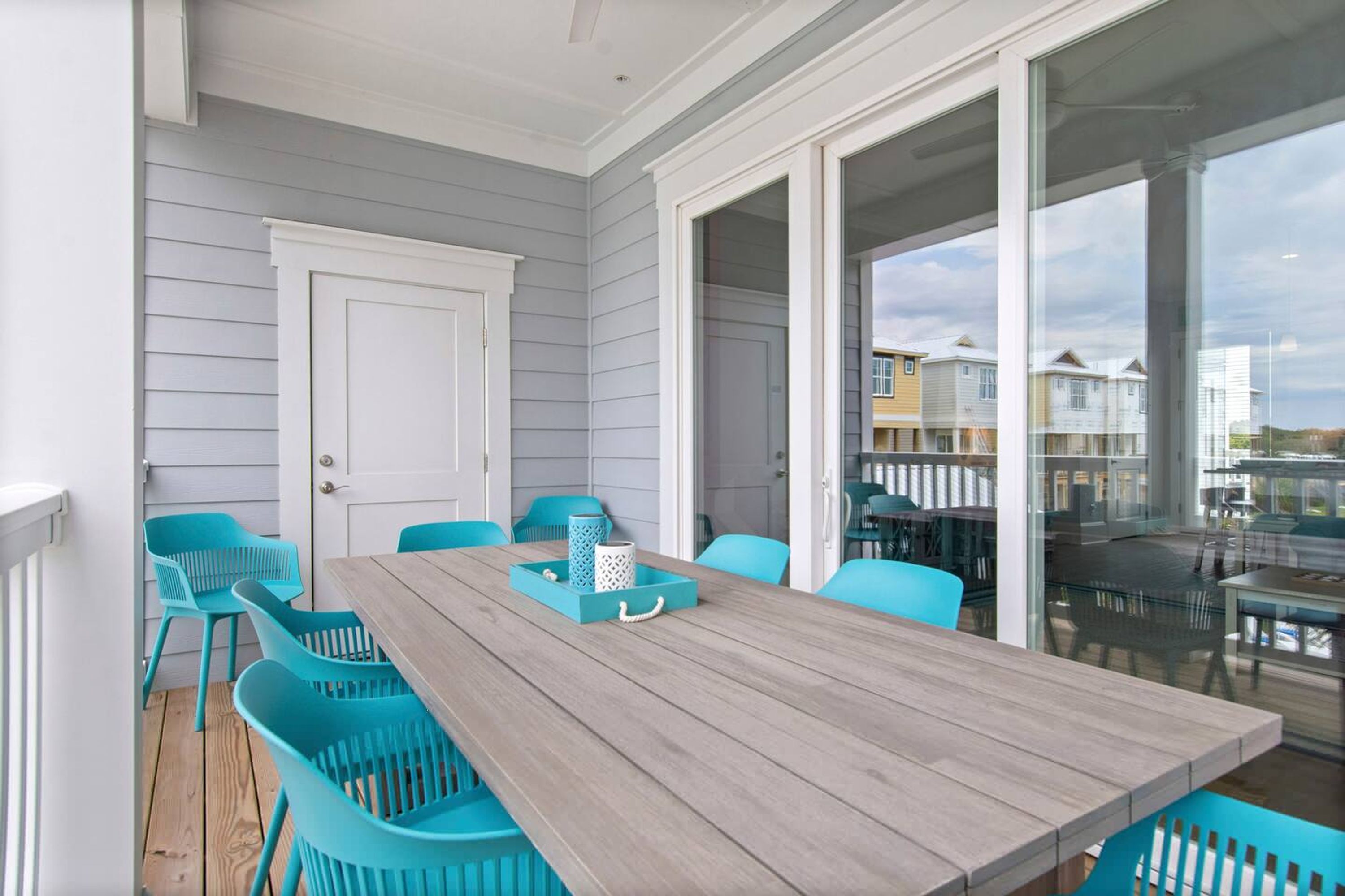 A covered patio with a wooden table and turquoise chairs, overlooking a residential area.