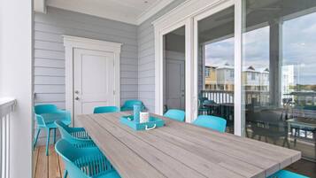 A covered patio with a wooden table and turquoise chairs, overlooking a residential area.