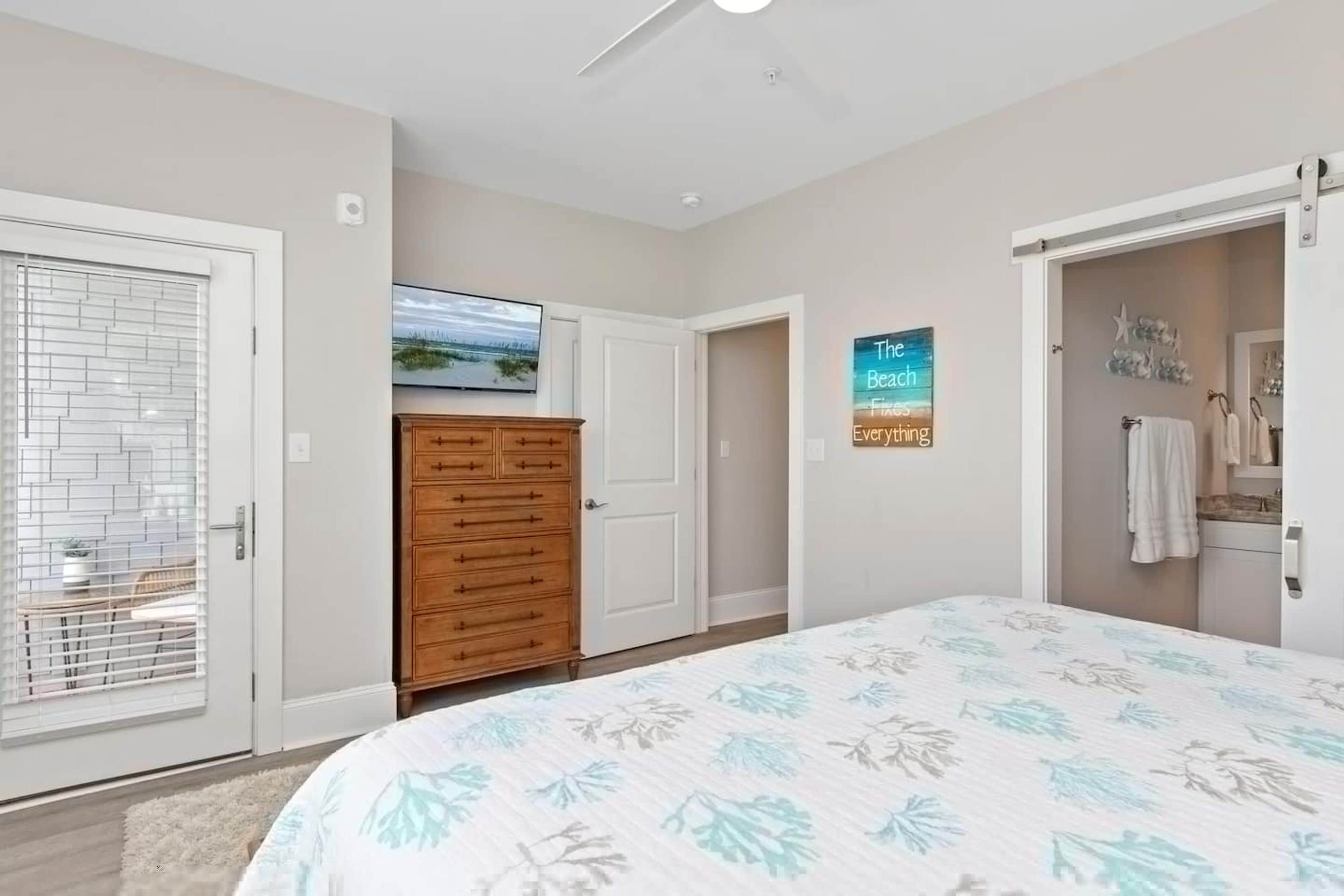 A bedroom with a bed, a dresser, a door, and a wall with a picture and a sign.