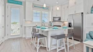 Une cuisine moderne avec des meubles blancs, un îlot central doté de tabourets de bar, des appareils en acier inoxydable et une enseigne indiquant « Emerald Isle ».