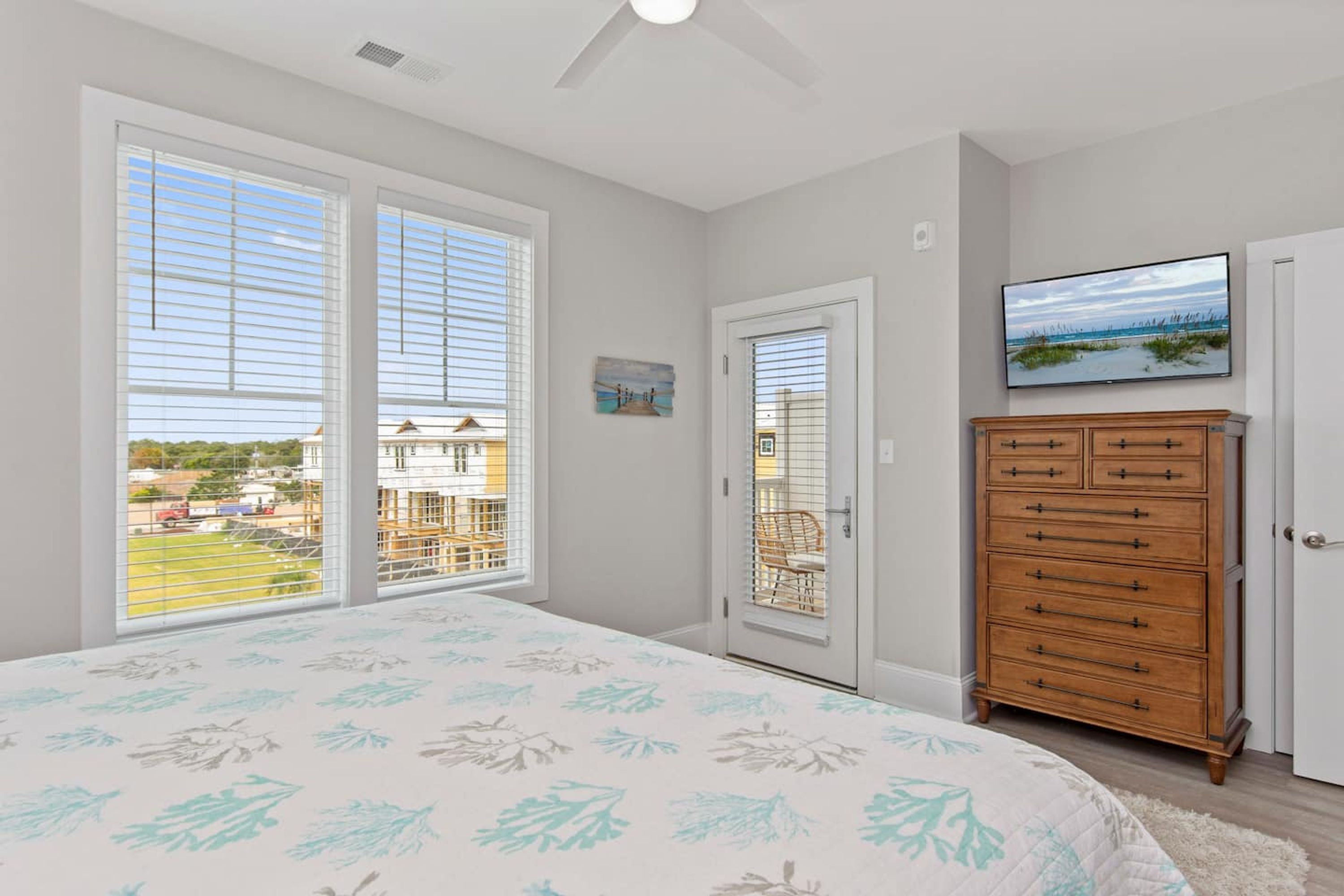 A bedroom with a large bed, a dresser, a television, and a door leading to a balcony.