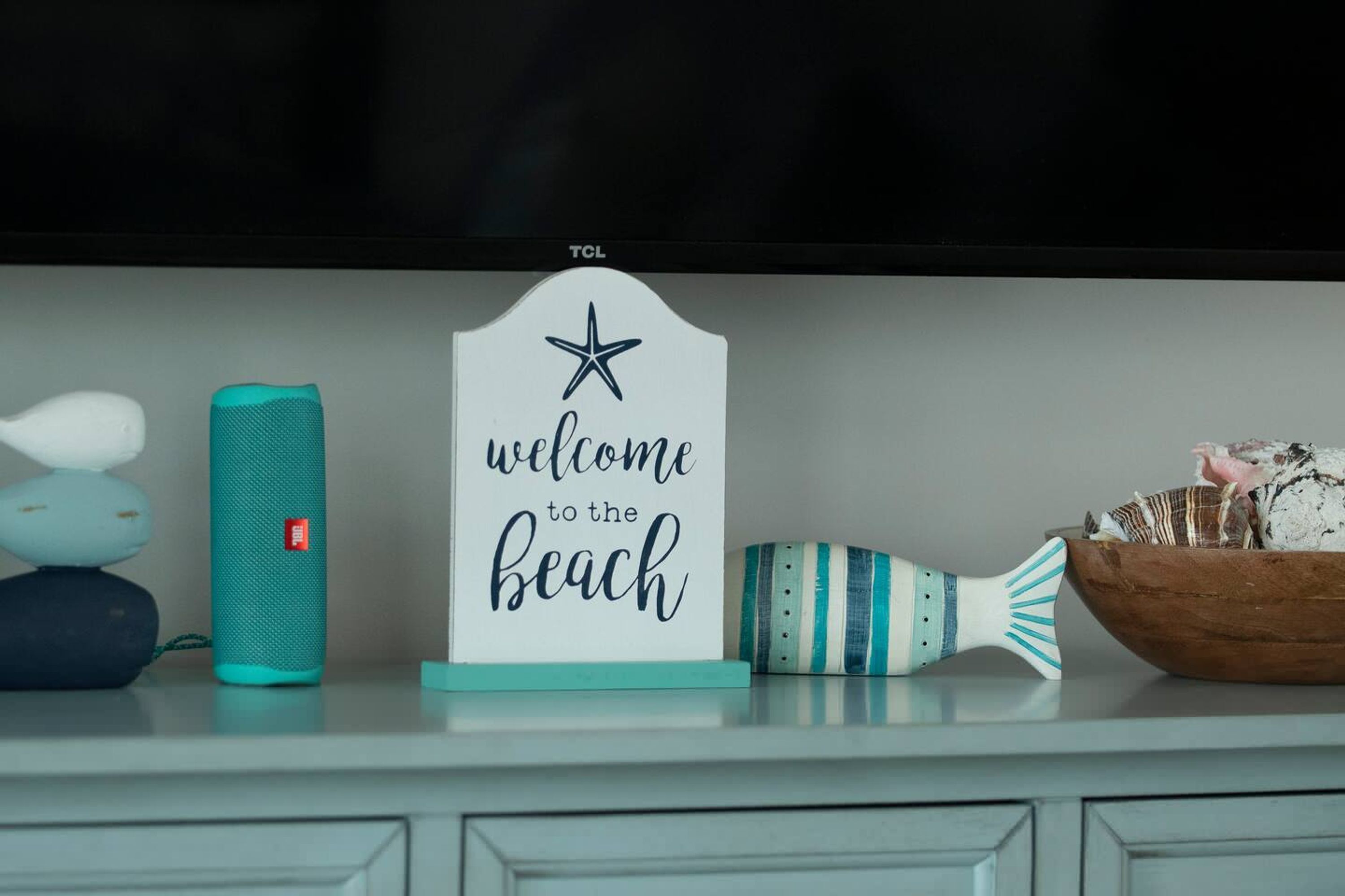 Una repisa con un cartel que dice 'bienvenidos a la playa', un altavoz color turquesa y un adorno a rayas.
