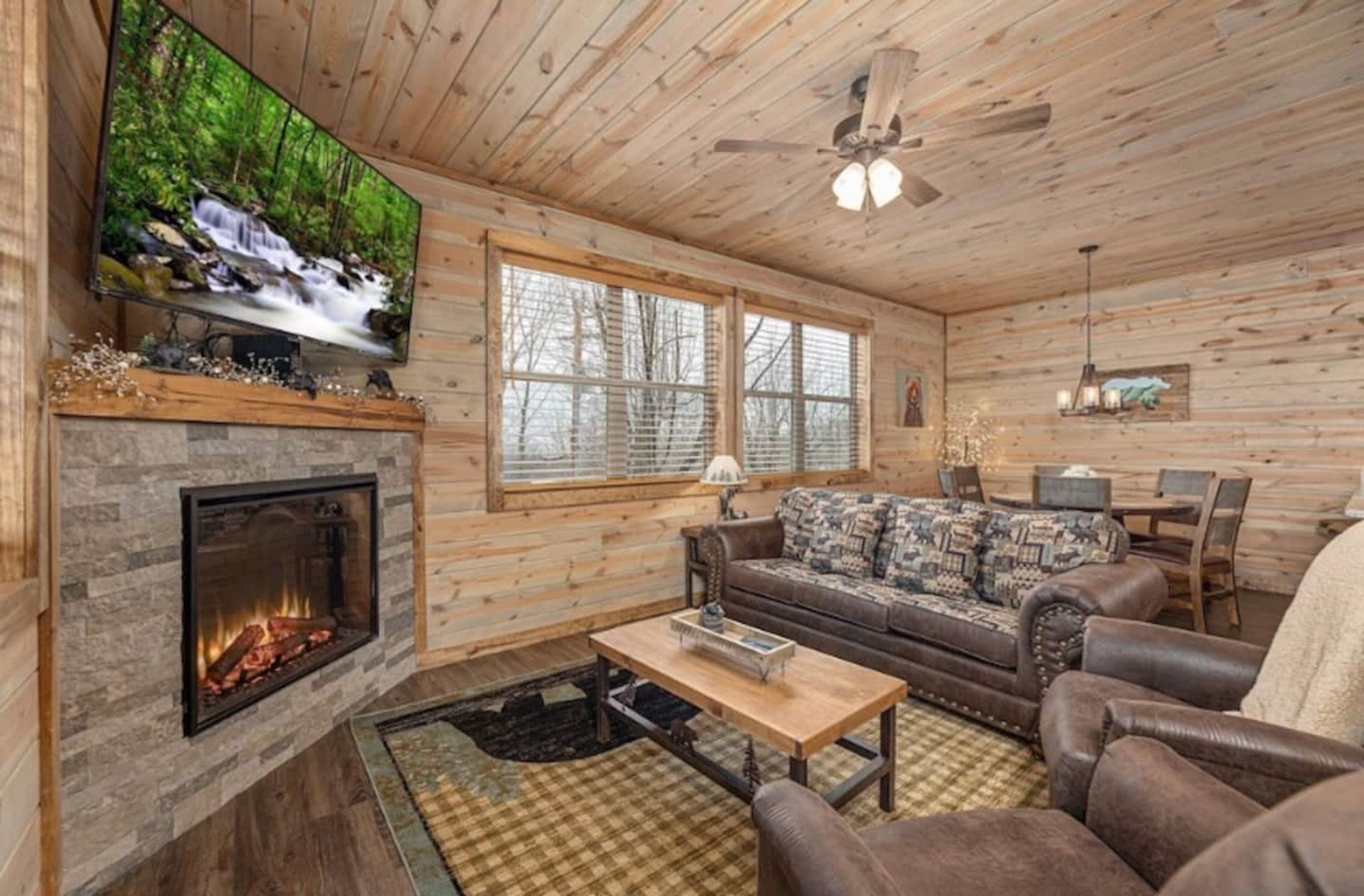 A cozy cabin interior with a fireplace, a television mounted on the wall, a sofa, and a dining area.