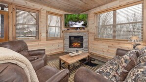 A cozy cabin interior with wooden walls, a fireplace, leather sofas, and a television mounted above the fireplace. - Lux Cabin Smoky Mtn View Dog Friendly Hot Tub (Gatlinburg)