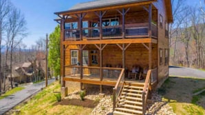 A two-story wooden cabin with a balcony on the upper floor, a front porch, and a staircase leading to the entrance. - Lux Cabin Smoky Mtn View Dog Friendly Hot Tub (Gatlinburg)