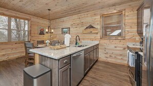 A wooden cabin interior with a kitchen featuring a granite countertop, stainless steel appliances, and a large window. - Lux Cabin Smoky Mtn View Dog Friendly Hot Tub (Gatlinburg)