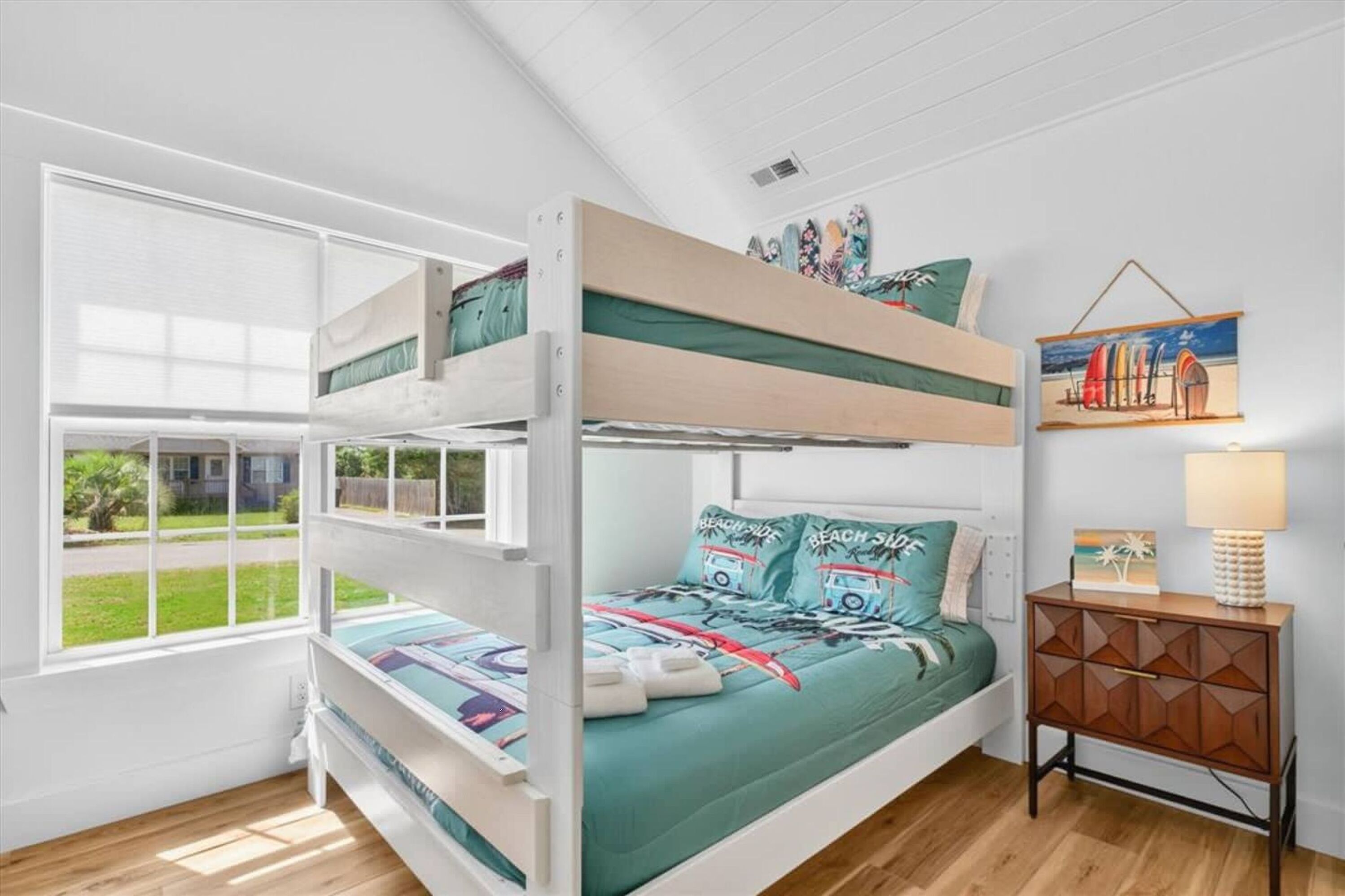 A bunk bed room with a view of the outdoors, a small cabinet, and a painting on the wall.